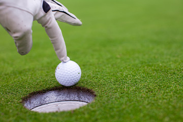 Man's hand putting a golf ball into a hole on the green field
