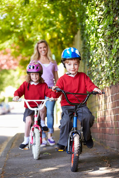 Children Riding Bikes On Their Way To School With Mother