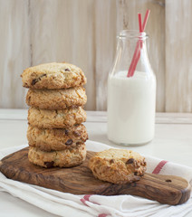 Chocolate chip cookies on cooking board and bottle of milk.