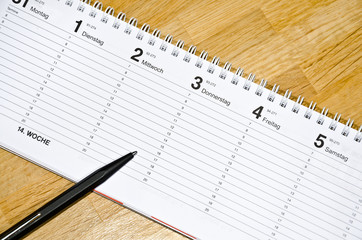 Schwarzer Stift liegt auf Termin-Kalender auf schickem Holztisch