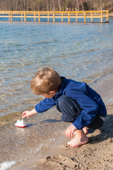 Kleiner Junge spielt am Seeufer mit einem Spielzeugschiff
