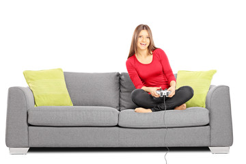 Obraz premium Young smiling female sitting on a sofa and playing video games
