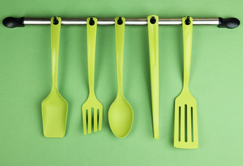 Plastic kitchen utensils on silver hooks on green background