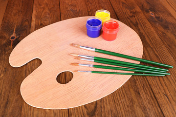 Wooden art palette with paint and brushes on table close-up