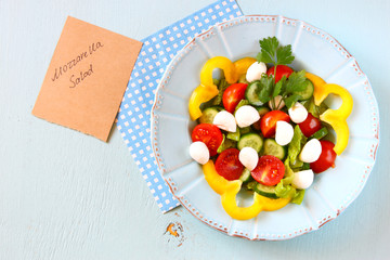 salad with mozzarella and fresh vegetables on wooden table backg