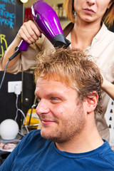 Beautiful man at the hairdresser blow drying his hair