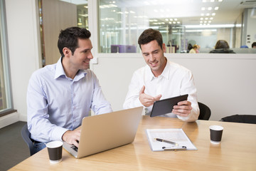Two casual businessmen working together in office with la