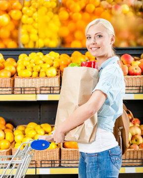 Girl with cart hands bag with fresh vegetables in the store