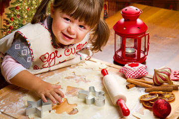 Little girl baking Christmas cookies cutting pastry with a cooki