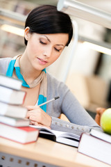 Woman with green apple surrounded with piles of books reads