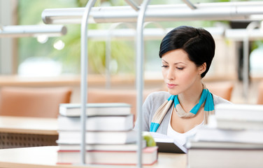 Woman surrounded with piles of books reads sitting at library