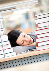 Female student sleeping at the desk with piles of books