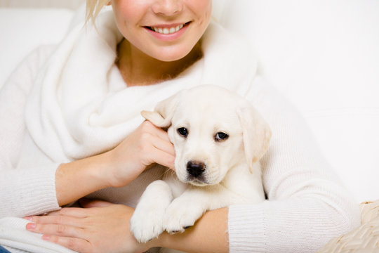 Woman in white holds white labrador puppy on her hands