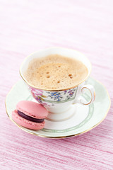 Pink macaroon on a saucer with cup of coffee