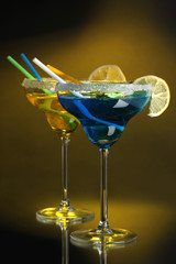 Yellow and blue cocktails in glasses on color background