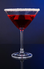 Red cocktail in martini glass on dark blue background