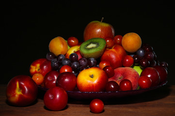 Fototapeta na wymiar Assortment of juicy fruits on wooden table, on dark background