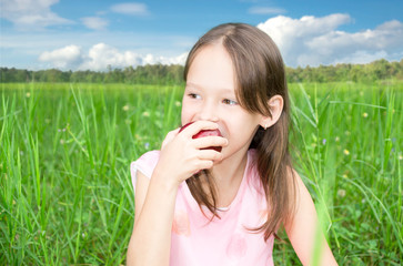 Cute little girl sitting in high grass and eating apple
