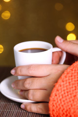 Hands holding mug of hot drink, close-up, on bright background