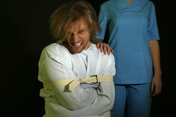 Mentally ill man in strait-jacket on black background