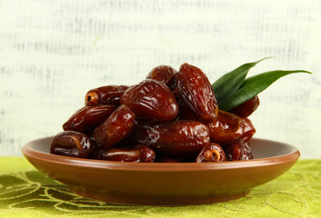 Dried dates on plate on tablecloth on wooden background