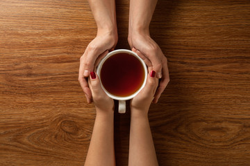 woman and man hands holding hot cup of tea on wooden table