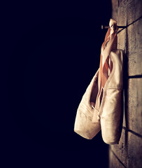 Used ballet shoes hanging on wooden background