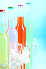 Drinks in glass bottles with ice cubes on blue background