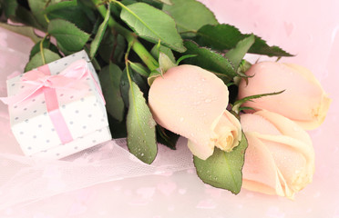 Beautiful roses and gift on pink cloth, close up