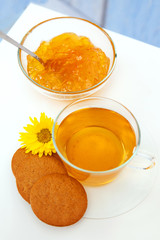The cap of tea and orange jam on white table