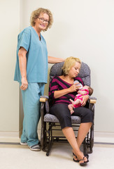 Nurse Standing By Mother Feeding Newborn Babygirl In Hospital