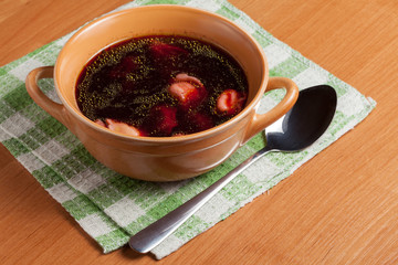 Red borscht with ravioli on a wooden board.