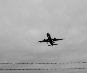 Flugzeug fliegt über Stacheldrahtzaun
