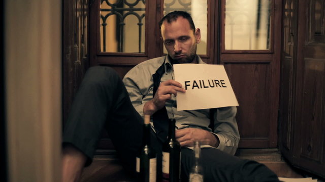 Drunk businessman showing failure sign, sitting on the floor