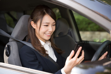 車でスマートフォンを見る女性　ビジネス