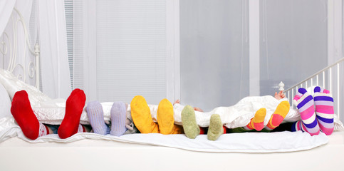 Happy family in colorful socks on white bed.