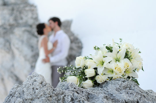 Bouquet and wedding couple kissing behind