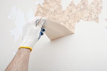 Hand removing wallpaper from wall