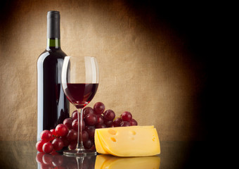 Bottle of red, a bunch of red grapes and a piece of cheese