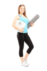 Smiling female athlete holding a weight scale and mat