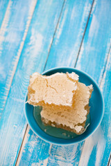 Saucer with honeycomb pieces, blue wooden background, copy space
