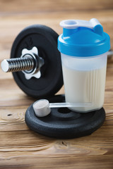 Vertical shot of protein shake, measuring scoop and a dumbbell