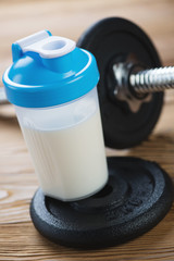 Building a muscle mass: protein drink and a dumbbell, close-up