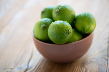 Glass bowl with ripe limes on a wooden surface, horizontal shot