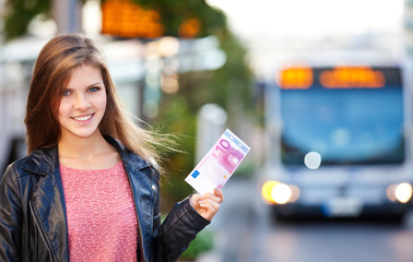 Mädchen an einer Bushaltestelle hält 10 Euro