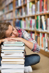 Napping student sitting on library floor leaning on pile of book