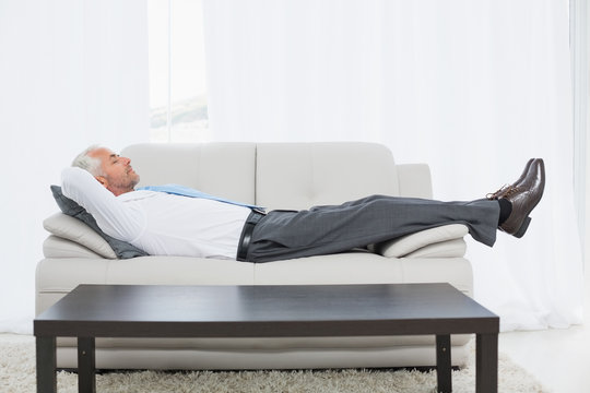 Tired mature businessman sleeping on sofa in living room