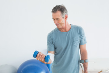 Smiling mature man with crutch and dumbbell