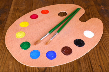 Wooden art palette with paint and brushes on table close-up