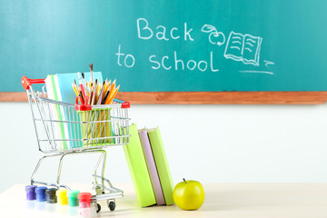 School supplies in supermarket cart on blackboard background